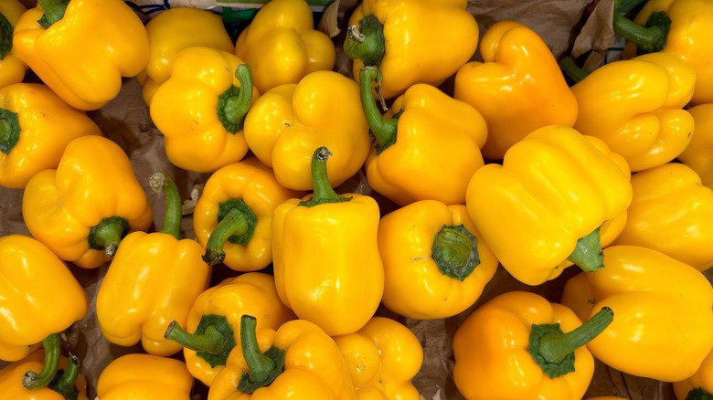A pile of yellow bell peppers with green stems on top of brown paper.