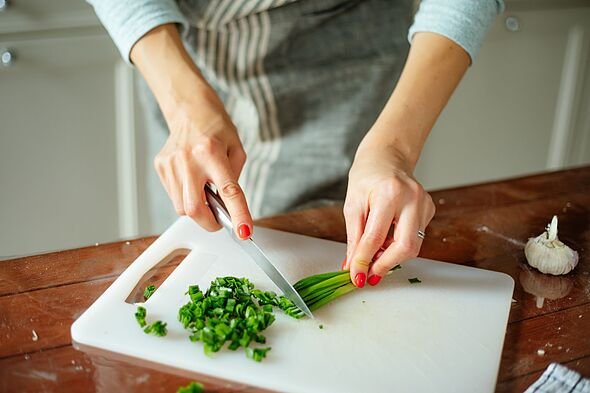Close up of female hands cutting scallions in pieces on white cutting board with kitchen knife