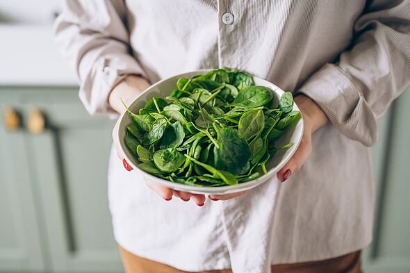 Green vegan breakfast meal in bowl with spinach, arugula, avocado, seeds and sprouts. Girl in leggins holding plate with hands visible, top view. Clea